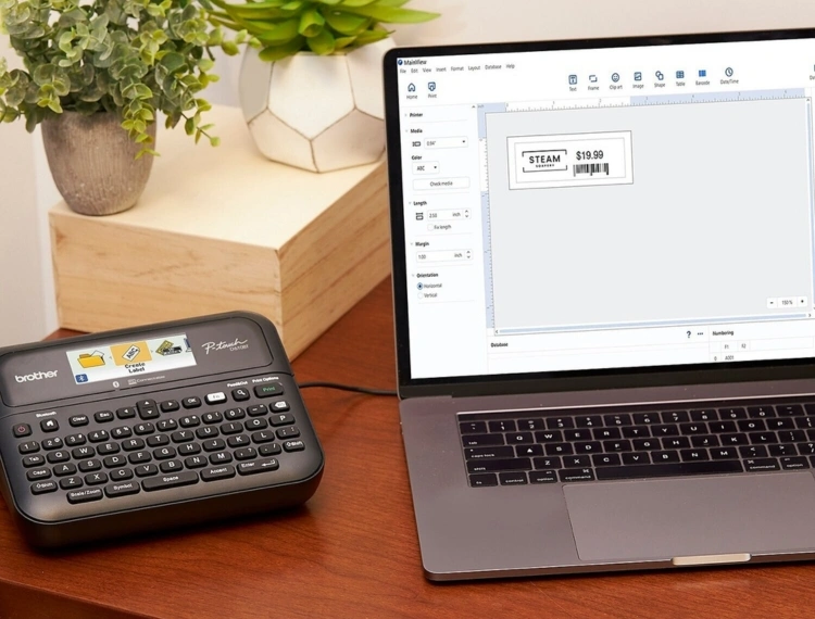 เครื่องปริ้นฉลาก Brother P-Touch วางอยู่ข้างโน๊ตบุ๊คที่กำลังแสดงหน้าจอการออกแบบฉลาก
